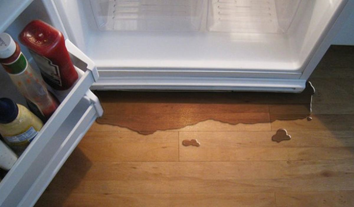 Water leaking from beneath a refrigerator onto a floor