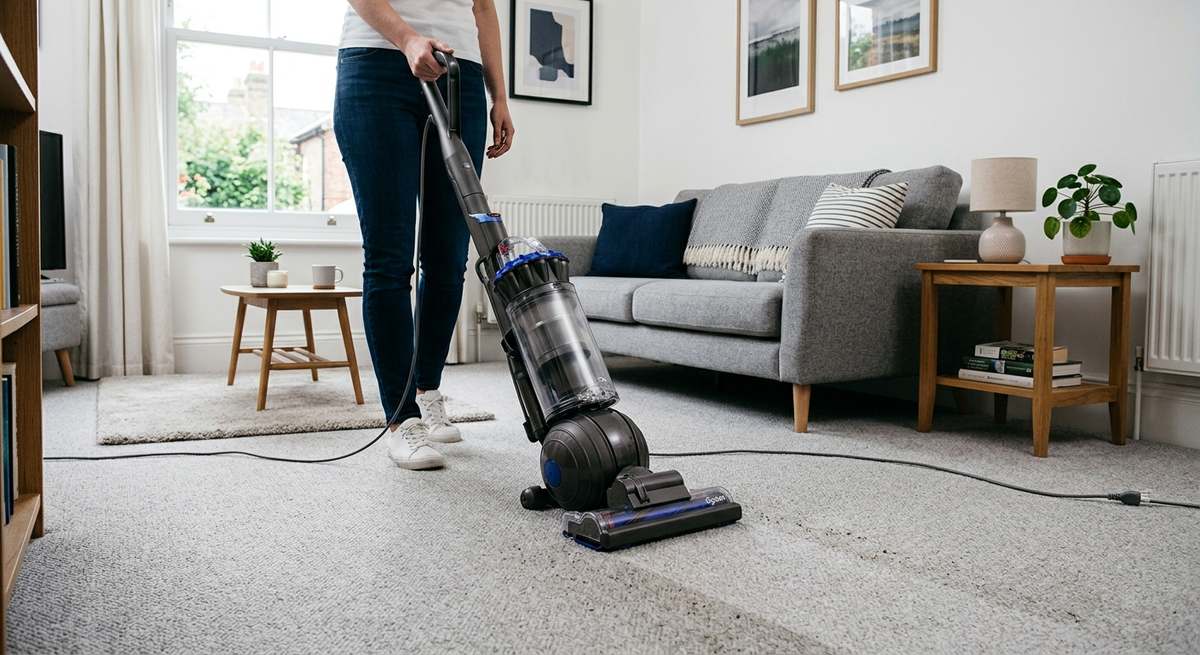 A vacuum cleaning a light carpet in a tidy small apartment living room